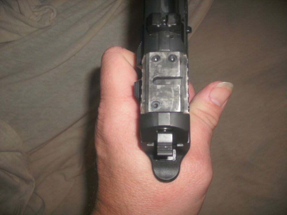 Hand holding a black handgun viewed end-on, no vehicle shown