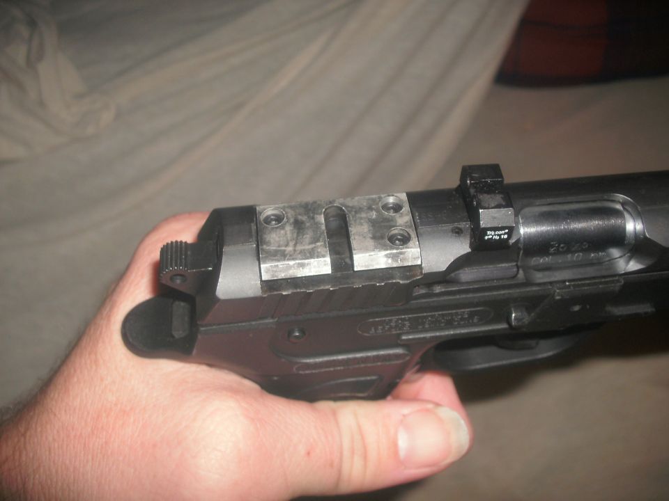 Hand holding a black semi-automatic pistol with a metal fixture on the slide indoors.