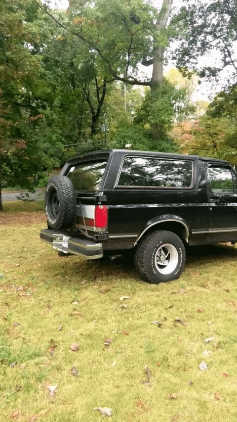 1988 Ford Bronco - The rear view of a black 1988 Ford Bronco shows its spare tire mounted on the tailgate.