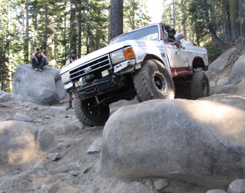 1984 Ford Bronco - A white and red Ford Bronco navigates a rocky trail in a wooded area.