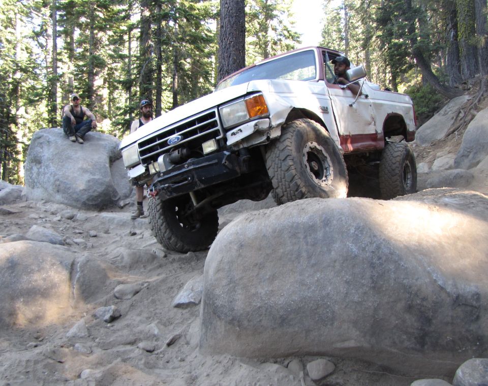 White and red Ford Bronco off-roading over rocks, front grille visible
