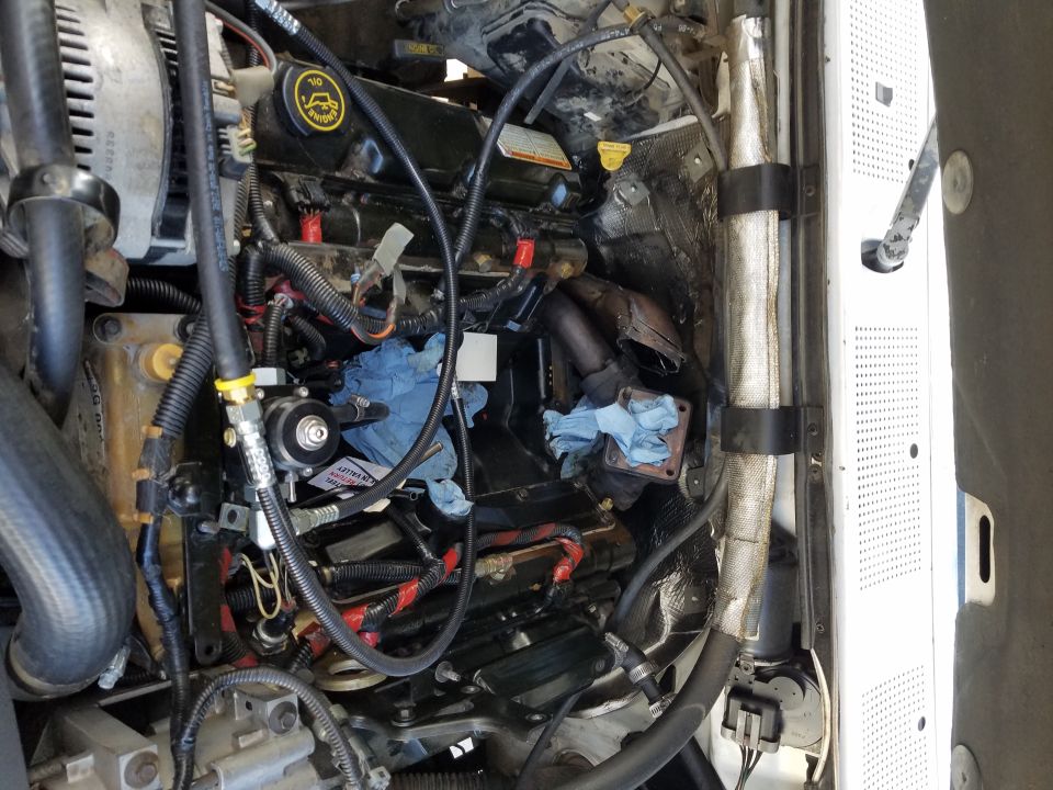 Close-up of a diesel engine bay with various hoses, wires, and engine components visible. Some blue shop towels are present