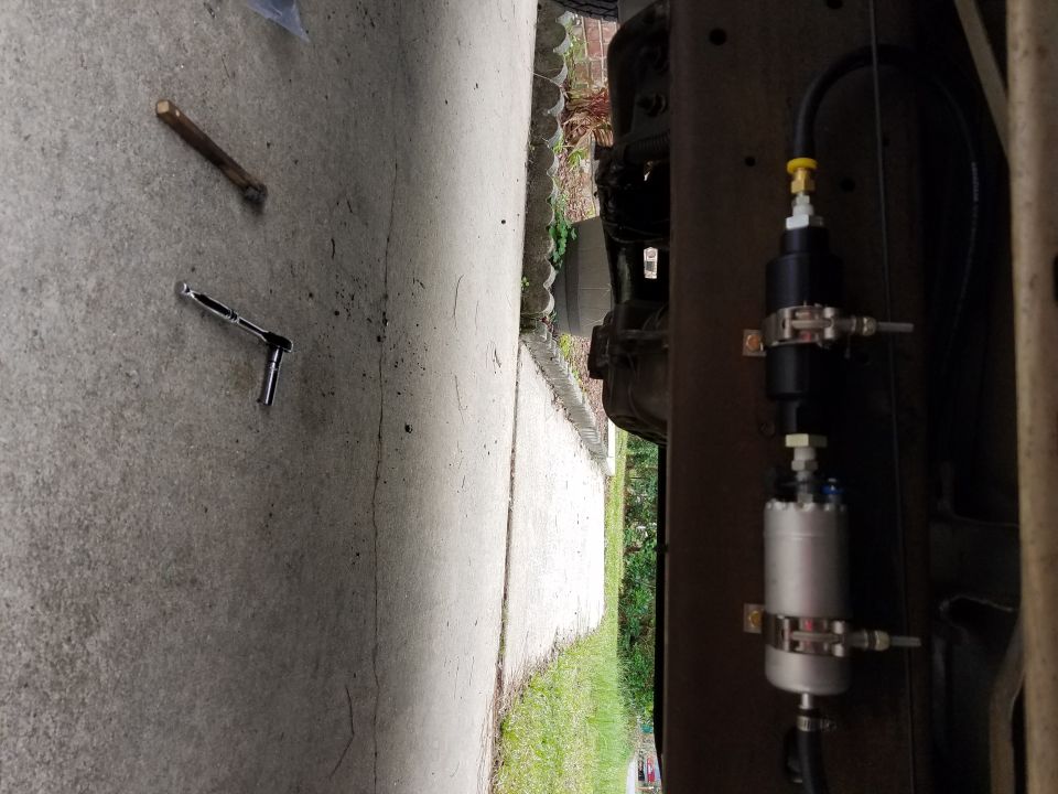 Fuel filter and pump assembly mounted on vehicle frame rail, with a ratchet and stick on the ground