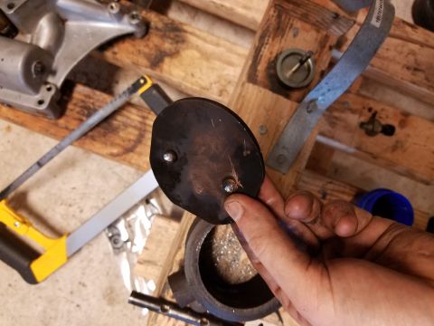 1995 Ford F-250 - A person is holding a metal plate, likely for an EBPV delete, with tools and wooden pallets in the background.