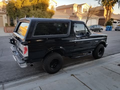 1993 Ford Bronco - This black Ford Bronco, likely a 1992 model, is parked curbside with a spare tire on the rear and aftermarket wheels.