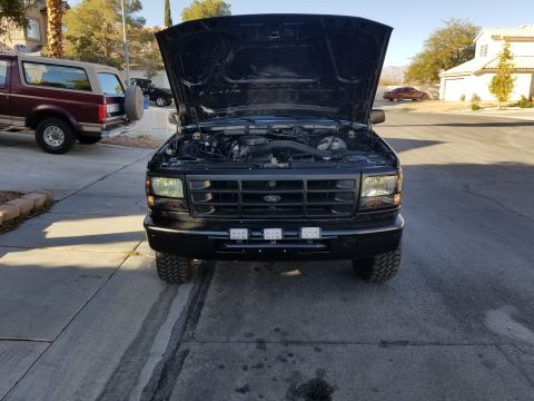 1993 Ford Bronco - Two Ford Broncos parked in a driveway, one with its hood open revealing the engine.