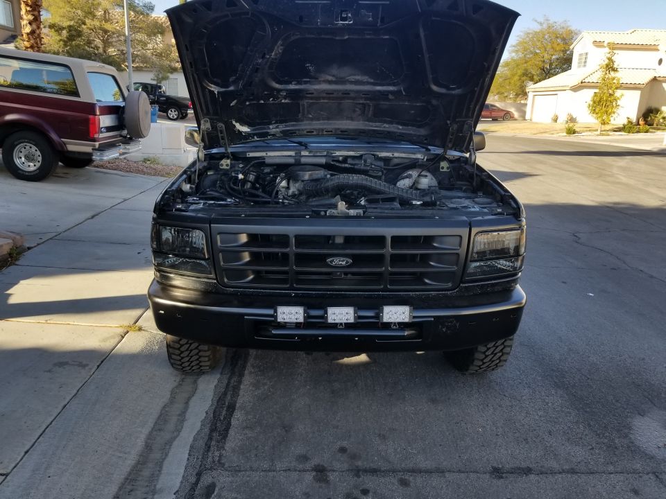 Black Ford F-Series truck with hood open, showing engine. Another maroon SUV is parked to the left