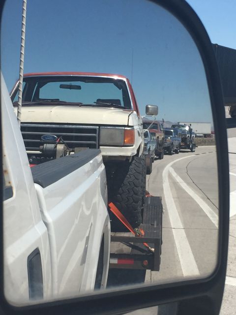 1984 Ford Bronco - A line of trucks, including a lifted Bronco, are seen on the road.