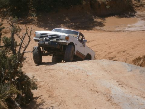 1984 Ford Bronco - This lifted Ford truck navigates a steep sandy incline, showing its off-road capabilities.