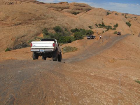 1984 Ford Bronco - Several off-road vehicles navigate a dusty, rocky terrain under a clear blue sky.