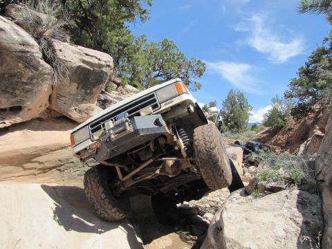 1984 Ford Bronco - A white 1984 Ford Bronco tackles a challenging off-road course, with another vehicle visible further down the trail.