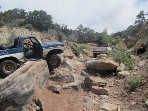 1984 Ford Bronco - Two trucks tackle a challenging rocky path in a desert landscape.