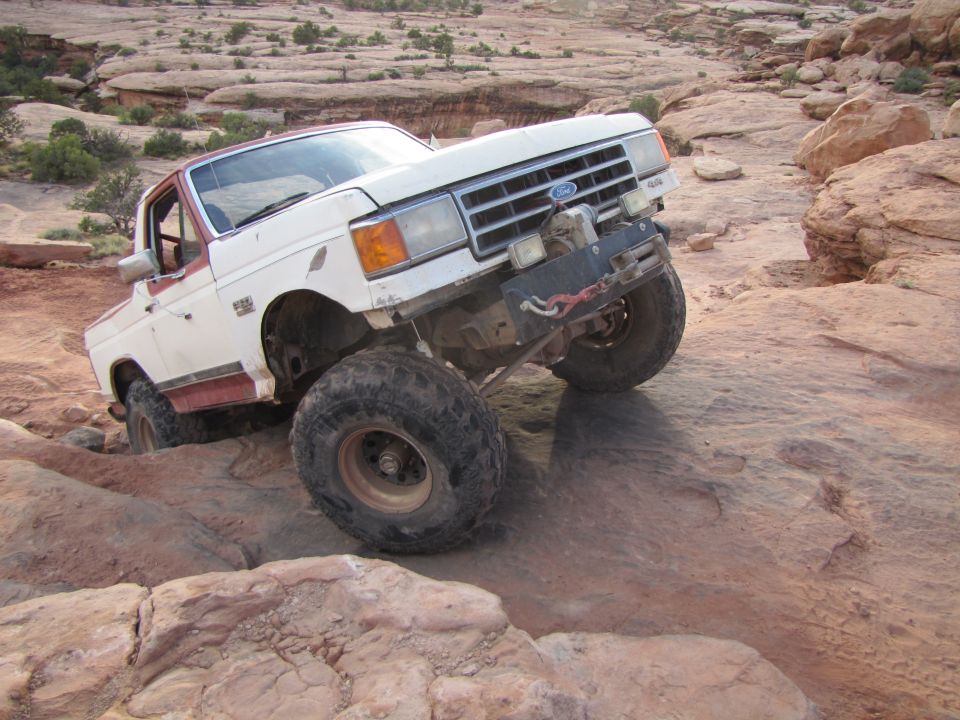 White Ford Bronco with red trim driving over rocks off-road
