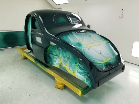 1940 Ford Coupe - A dark green car body, masked for painting, sits on a yellow stand in a paint booth.