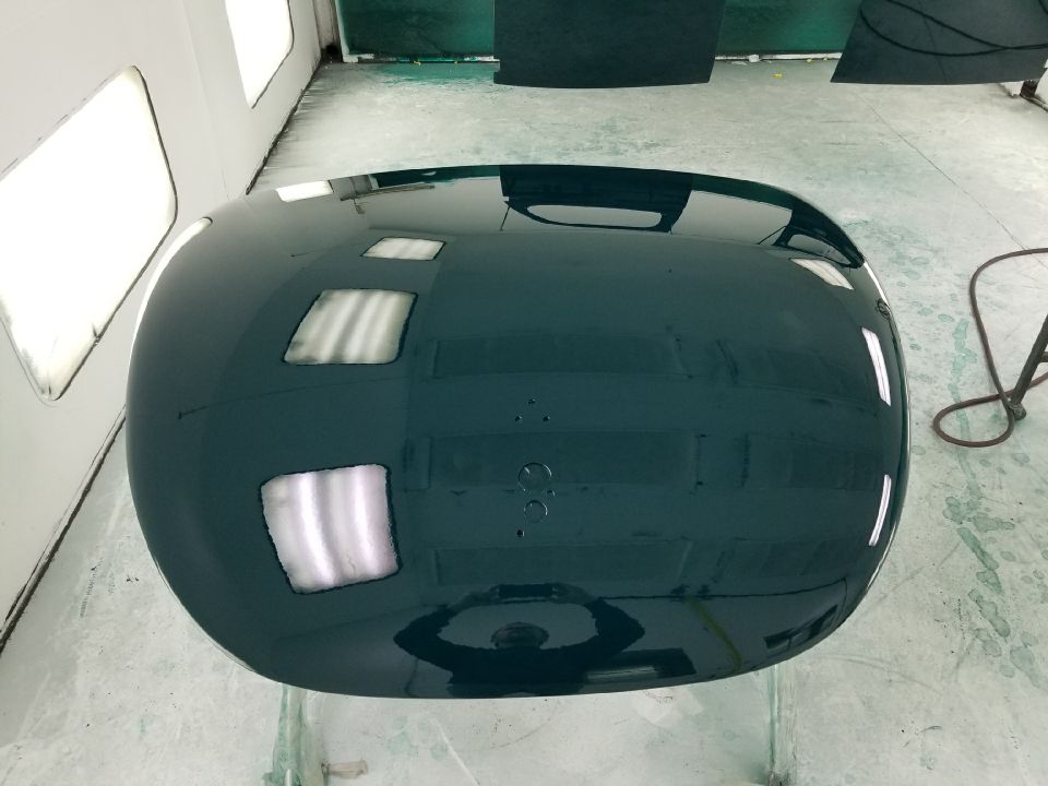 Dark green car hood reflecting overhead lights and a person holding a camera