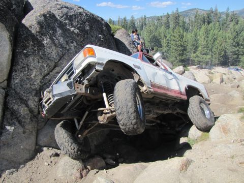 1984 Ford Bronco - This modified truck is navigating a challenging rocky terrain, with one wheel lifted high.