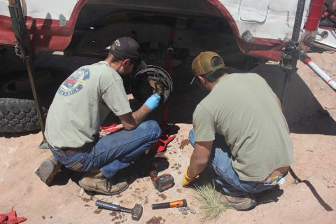 1984 Ford Bronco - Two mechanics are seen performing maintenance on the brake system of a vehicle, which is supported by a jack.