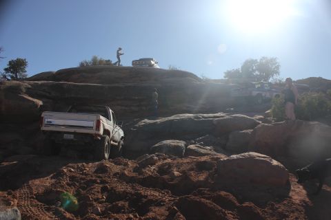 1984 Ford Bronco - A white Ford Bronco navigates a challenging rocky trail with other vehicles in the background under a bright sun.