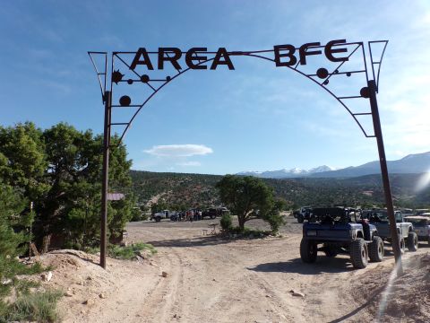 1984 Ford Bronco - Several off-road vehicles are gathered under the "AREA BFE" arch in a mountainous, arid landscape.