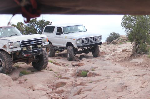 1984 Ford Bronco - Two modified Ford Broncos navigate a challenging rocky off-road course. The lead vehicle's grille suggests a 1978 model year.