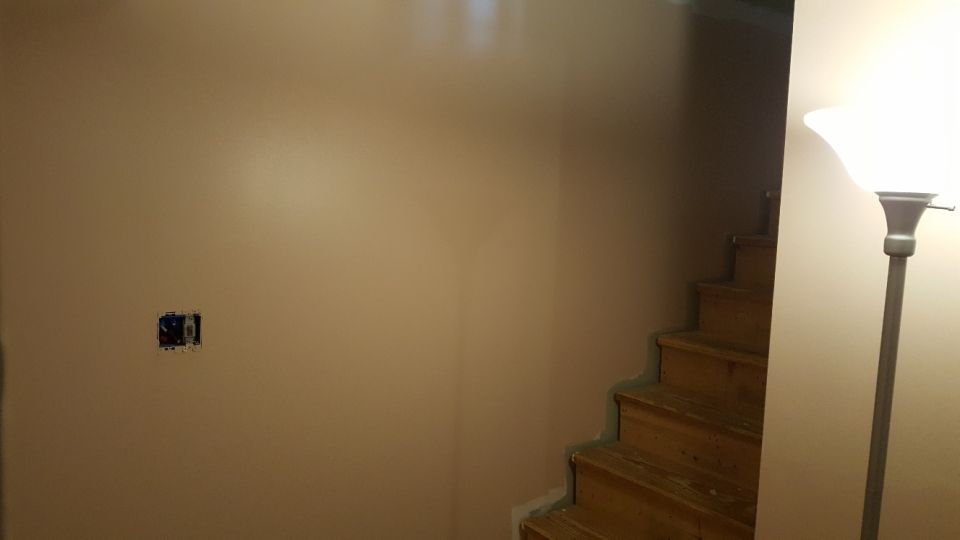 Interior wall with an electrical box and a wooden staircase leading upwards. A floor lamp is on the right