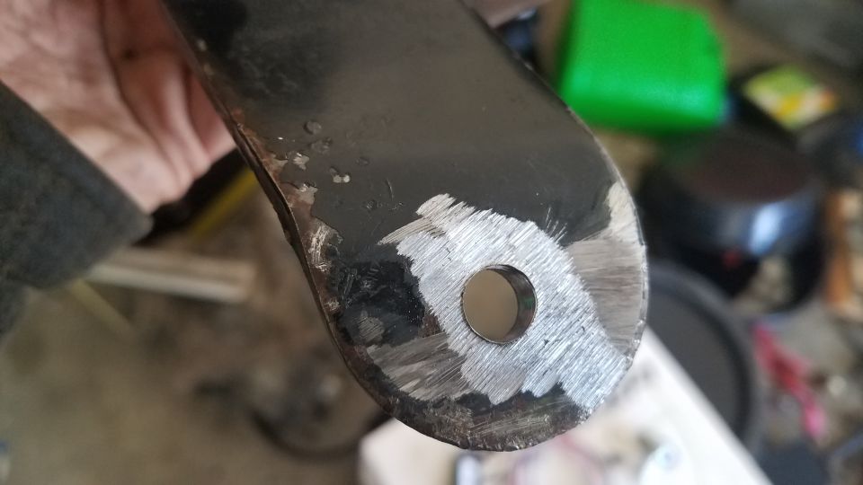 Close-up of a metal bracket with a hole, showing grinding marks and some rust spots