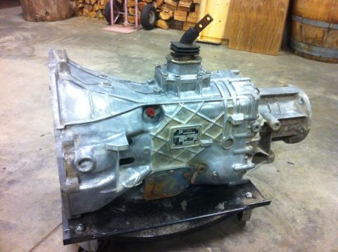 1978 Ford Bronco - A silver transmission with a shifter is shown mounted on a stand in a workshop setting.