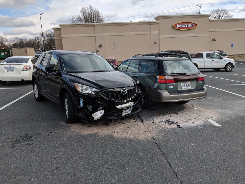 Black Mazda CX-5 with front-end damage parked next to a damaged Subaru Outback wagon