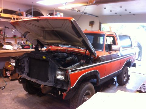 1978 Ford Bronco - The front end of an orange Ford Bronco is being worked on in a garage.