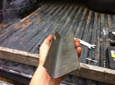 1978 Ford Bronco - A metal bracket is held in a person's hand, with the bed of a truck and tools in the background.
