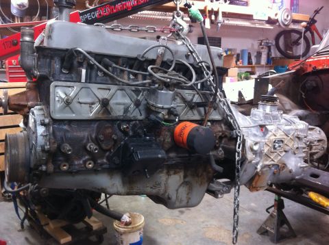 1978 Ford Bronco - Engine and transmission assembly being worked on in a garage setting, suspended by a hoist.