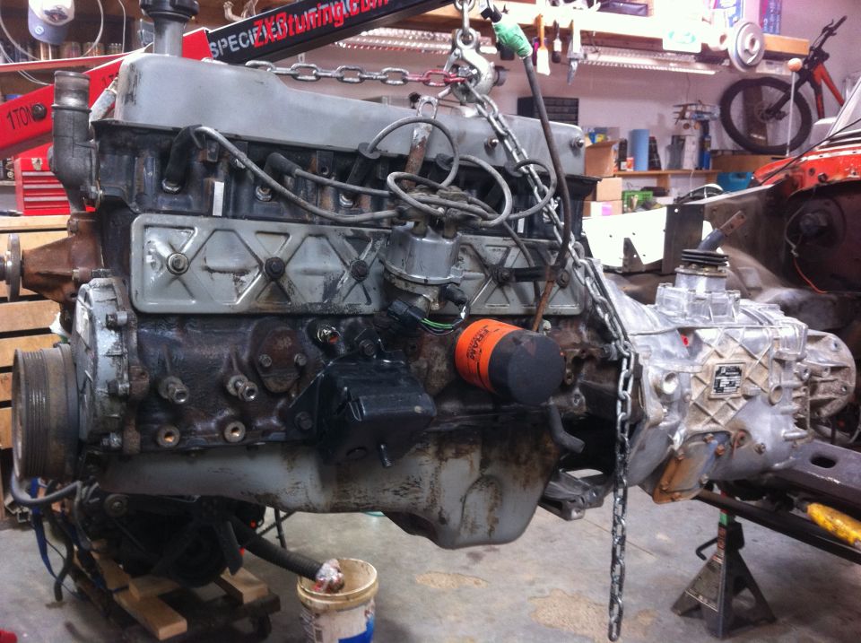 Engine and transmission assembly suspended by chains, with an orange oil filter visible