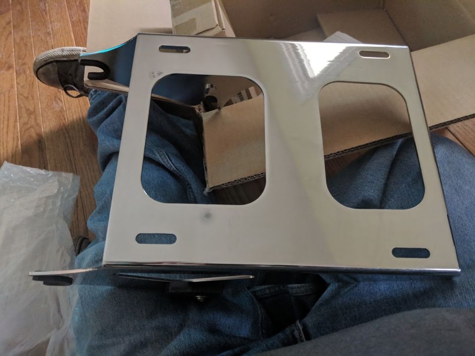 Chrome motorcycle luggage rack with two large cutouts, held by a person in jeans