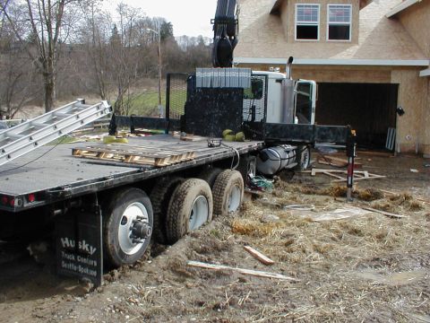 1983 Ford Bronco - A flatbed truck equipped with a crane is stuck in the mud at a construction site.