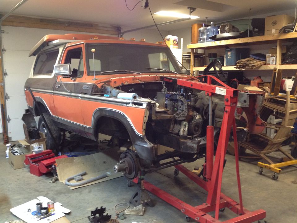1978 Ford Bronco with engine removed, supported by an engine hoist in a garage