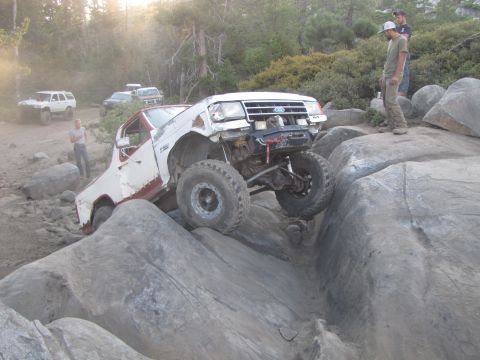 1984 Ford Bronco - Modified off-road truck navigates a rocky trail with other vehicles in the background.