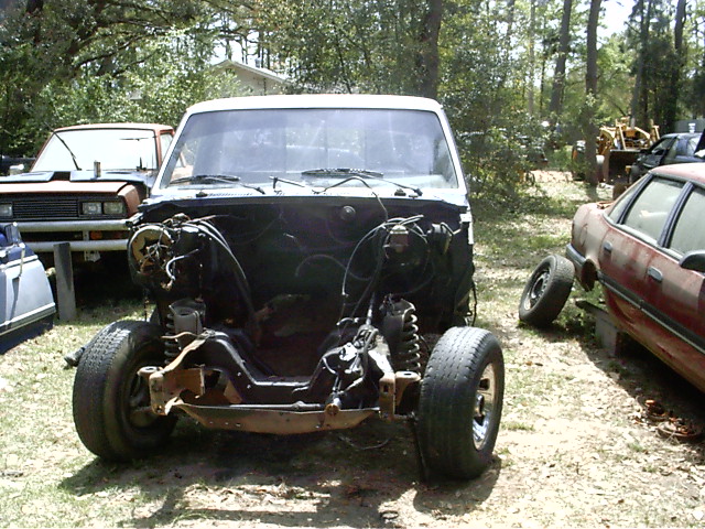 White truck chassis, front view, engine removed, tires on, parked outdoors