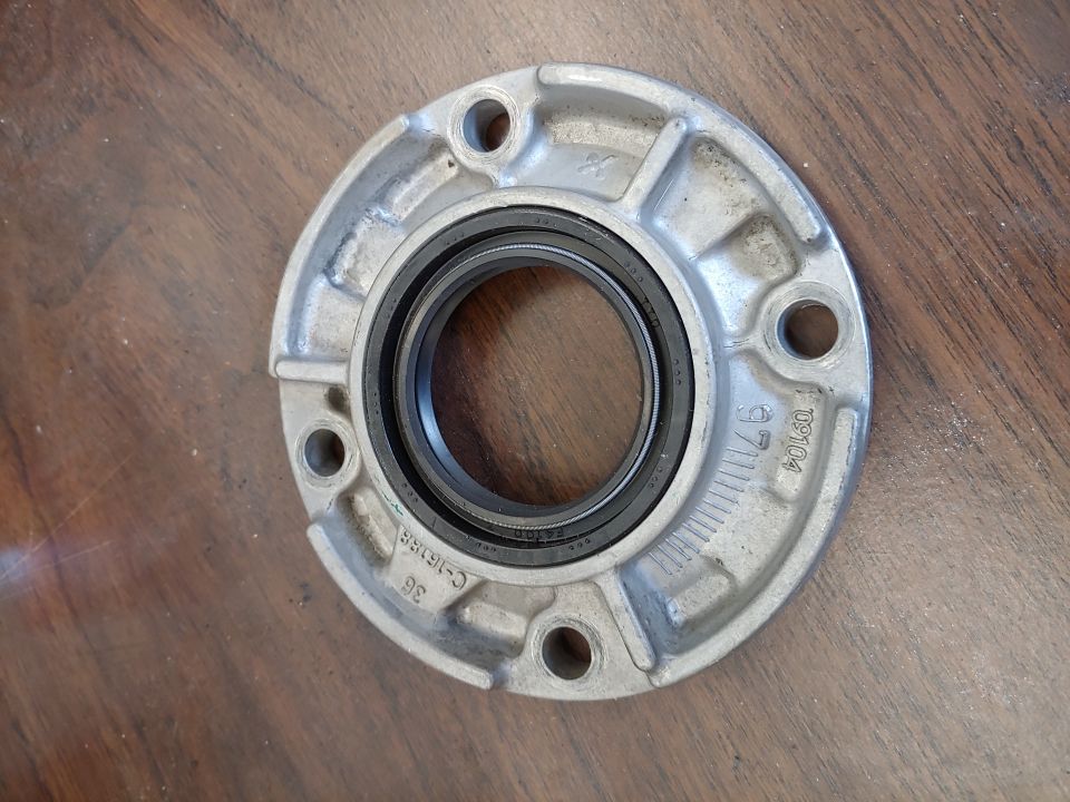 metal part with a black seal and bolt holes, sits on a wooden surface