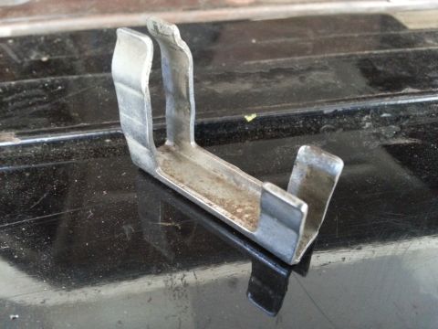1978 Ford Bronco - A close-up, angled shot shows a metal bracket with a U-shaped clip on one end. The bracket is resting on a dark, reflective surface with vi…