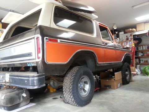 1978 Ford Bronco - Rear passenger side view of a lifted 1978 Ford Bronco in a garage, with the rear bumper removed and a fuel tank visible underneath. The veh…