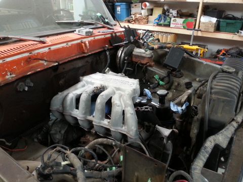 1978 Ford Bronco - The engine bay of a classic vehicle, likely a 1978 Ford Bronco, is shown with the hood removed. The image focuses on the intake manifold, e…