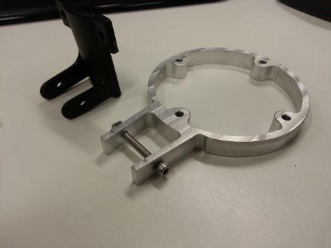1978 Ford Bronco - A black plastic bracket and a silver aluminum ring clamp with a bolt and nut are displayed on a white surface.