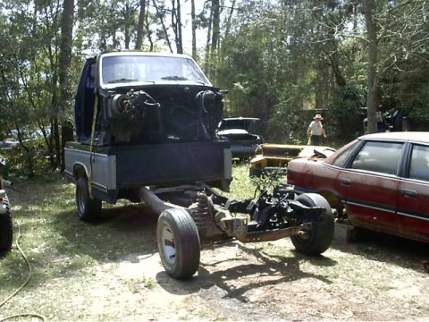 1985 Ford Bronco - Truck chassis with cab removed, parked outdoors next to other vehicles.
