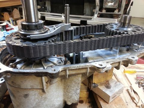 1978 Ford Bronco - A close-up view of a vehicle's transfer case with the chain and gears exposed. The transfer case housing is partially disassembled, resting…