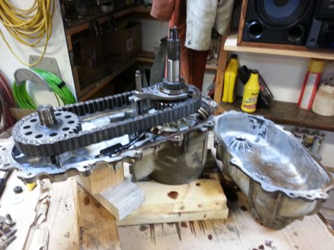 1978 Ford Bronco - A disassembled transfer case with a chain and gears is shown on a wooden surface. A separate aluminum oil pan sits to the right of the tran…