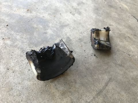 1989 Ford Bronco - Two pieces of burnt, melted material are lying on a concrete surface. The material appears to be black and white, with a shiny, melted text…
