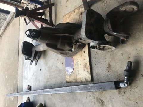 1989 Ford Bronco - A disassembled vehicle axle assembly is laid out on a concrete floor, resting on a wooden board. A long metal bar with a socket wrench atta…