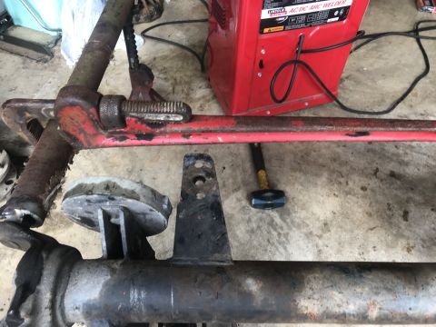 1989 Ford Bronco - A close-up view shows a rusty red pipe wrench clamped onto a metal bar, with a red Lincoln AC/DC Arc Welder and a sledgehammer visible in t…