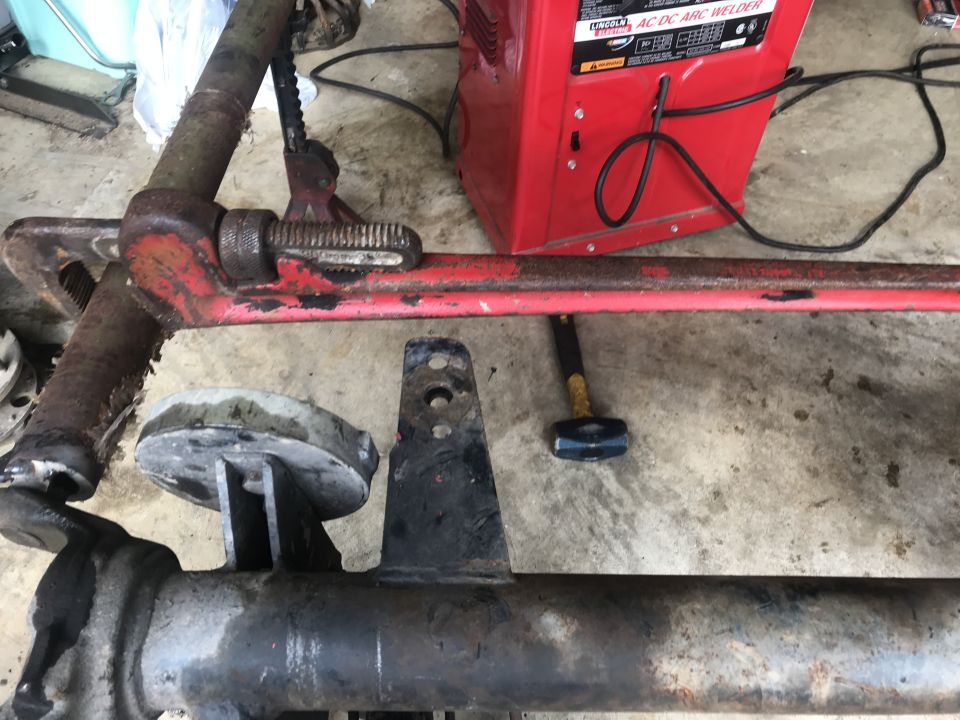 Rusty red pipe wrench on metal bar, Lincoln welder, sledgehammer