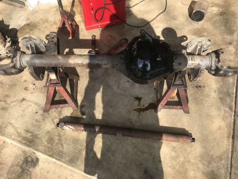 1989 Ford Bronco - A rear axle assembly with a differential cover painted black is supported by two red jack stands on a concrete surface. A separate drivesha…